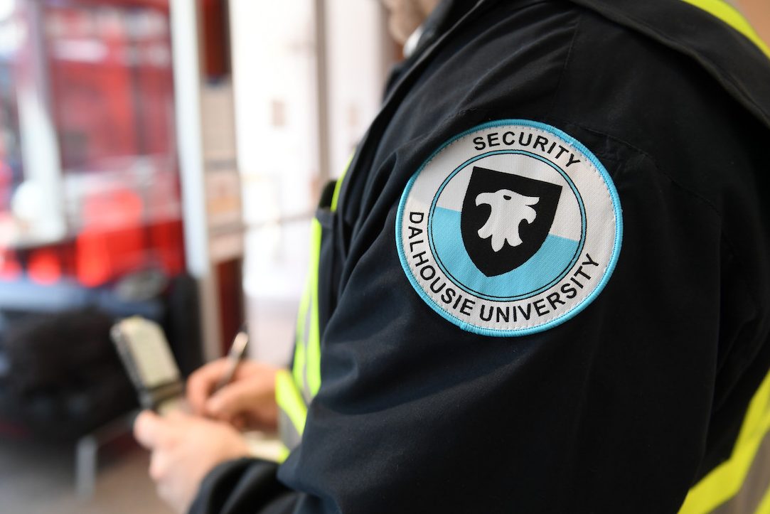 A guard wearing a badge that says "°ϲ Security" writes in a notepad. 